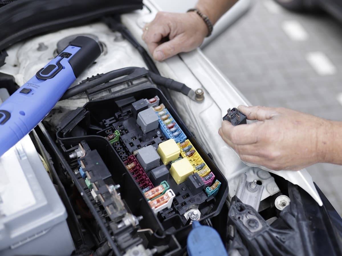 A mechanic working on a car's fuse box under the bonnet